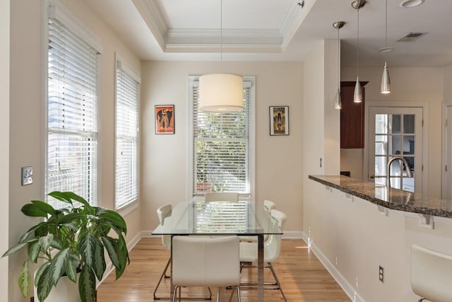 dining space with a tray ceiling, crown molding, sink, and light wood-type flooring