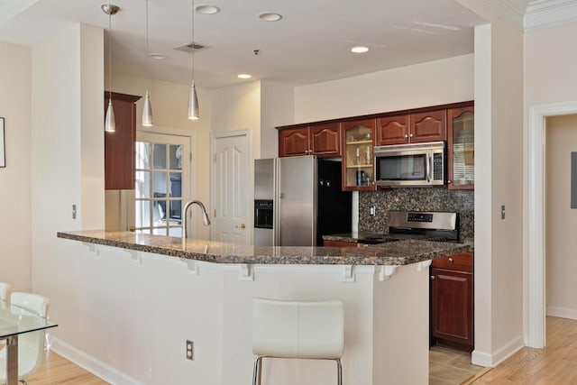 kitchen featuring pendant lighting, light hardwood / wood-style flooring, a kitchen bar, kitchen peninsula, and stainless steel appliances