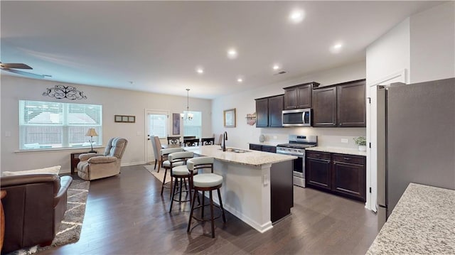 kitchen with dark brown cabinetry, appliances with stainless steel finishes, open floor plan, a kitchen breakfast bar, and a sink