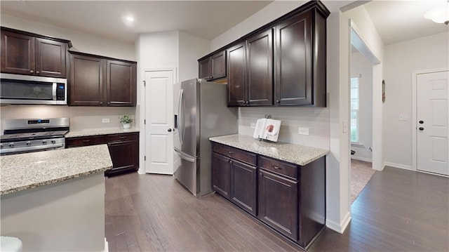 kitchen with dark wood-style flooring, dark brown cabinets, appliances with stainless steel finishes, light stone countertops, and tasteful backsplash