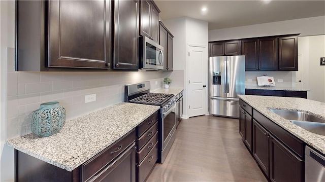 kitchen featuring tasteful backsplash, appliances with stainless steel finishes, light stone counters, dark brown cabinets, and recessed lighting