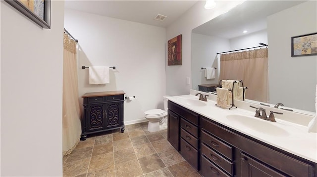 bathroom with toilet, double vanity, a sink, and visible vents