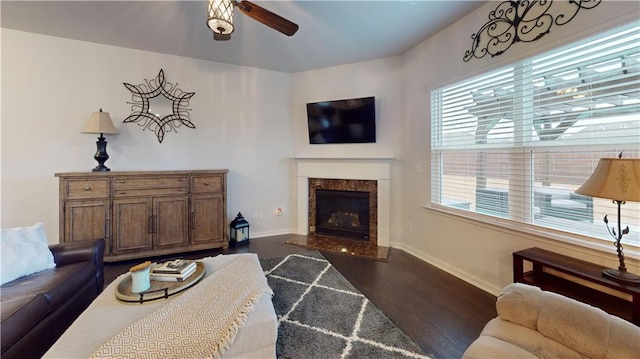 living room featuring a fireplace, dark wood finished floors, baseboards, and ceiling fan