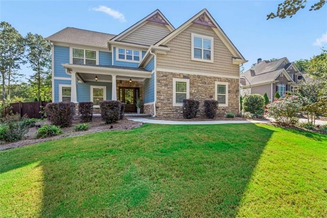 craftsman-style home featuring stone siding, fence, and a front lawn