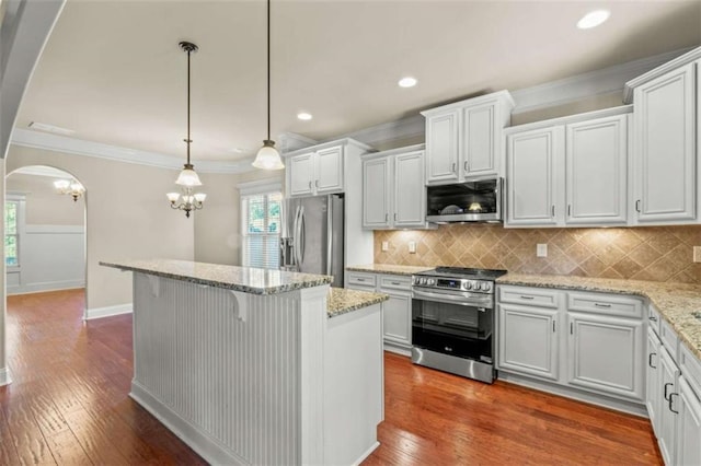 kitchen with arched walkways, white cabinets, appliances with stainless steel finishes, ornamental molding, and pendant lighting