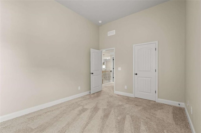 unfurnished bedroom featuring light carpet, baseboards, a towering ceiling, and visible vents