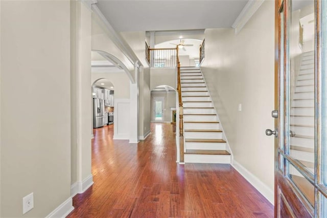 entryway with dark wood-type flooring, arched walkways, stairway, and baseboards