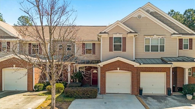 townhome / multi-family property with a standing seam roof, an attached garage, concrete driveway, brick siding, and metal roof