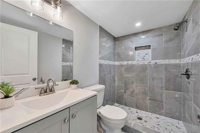 bathroom featuring vanity, a tile shower, and toilet