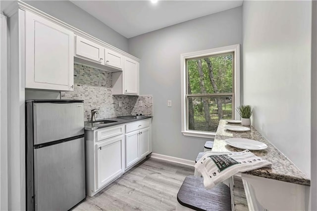 kitchen with white cabinetry, sink, backsplash, and stainless steel fridge