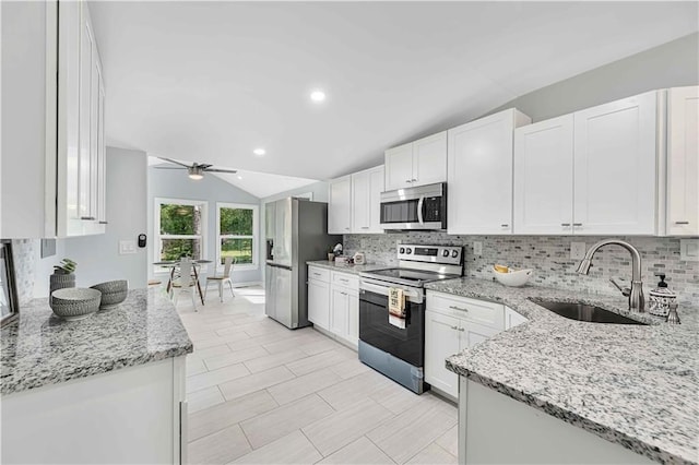 kitchen featuring vaulted ceiling, white cabinetry, sink, stainless steel appliances, and light stone countertops