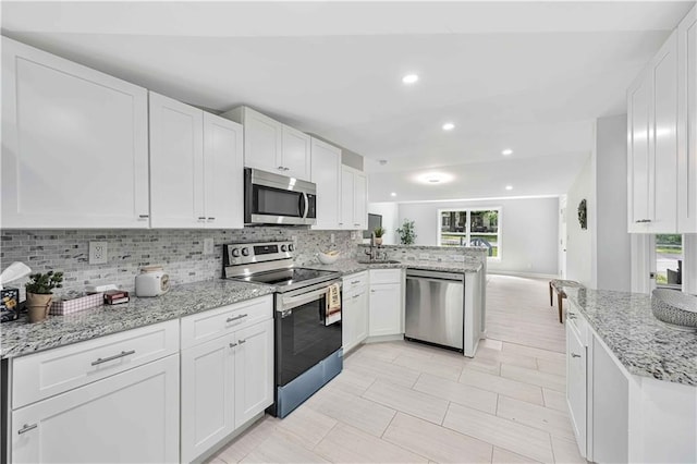 kitchen featuring appliances with stainless steel finishes, white cabinetry, light stone counters, tasteful backsplash, and kitchen peninsula