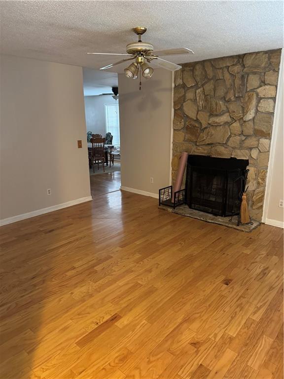 unfurnished living room with light hardwood / wood-style flooring, ceiling fan, a fireplace, and a textured ceiling