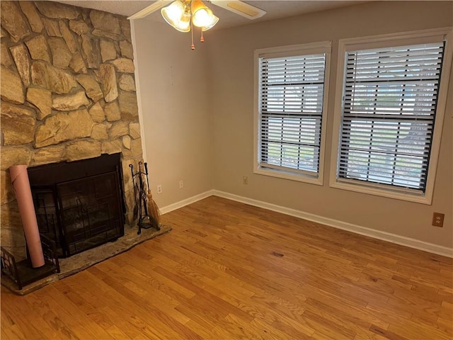 unfurnished living room with a stone fireplace, light hardwood / wood-style flooring, and ceiling fan