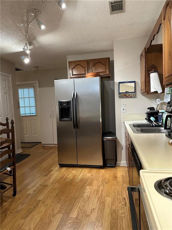 kitchen featuring sink, range, light hardwood / wood-style floors, stainless steel fridge with ice dispenser, and a textured ceiling