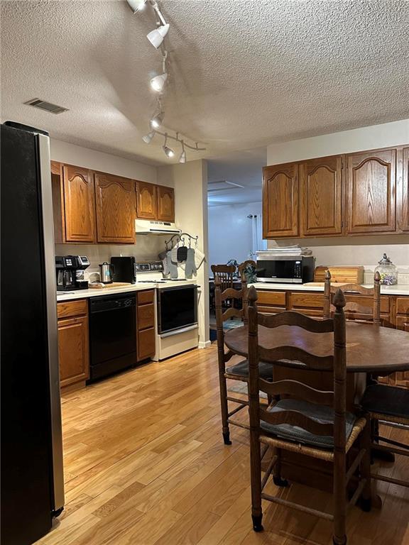 kitchen with appliances with stainless steel finishes, a textured ceiling, and light hardwood / wood-style floors