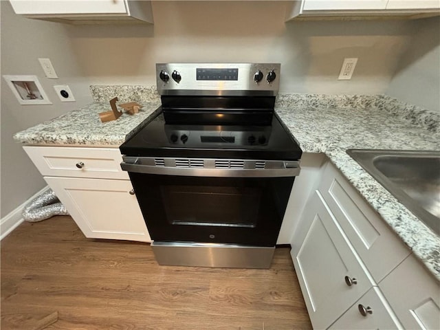 kitchen featuring light stone countertops, light hardwood / wood-style floors, stainless steel range with electric stovetop, and white cabinetry