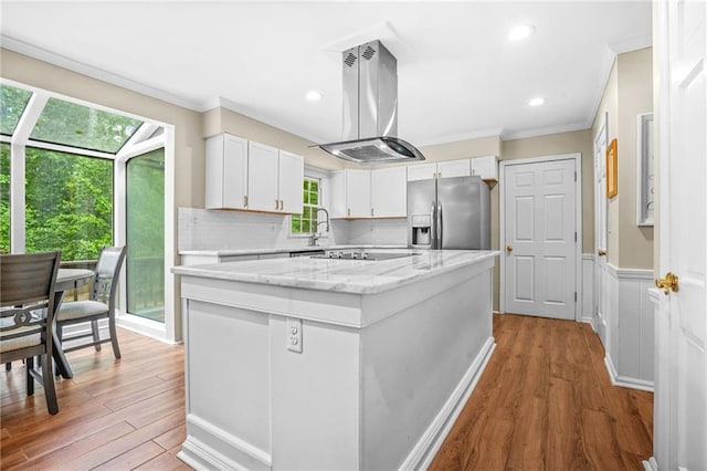kitchen featuring island exhaust hood, crown molding, stainless steel refrigerator with ice dispenser, a kitchen island, and black electric cooktop