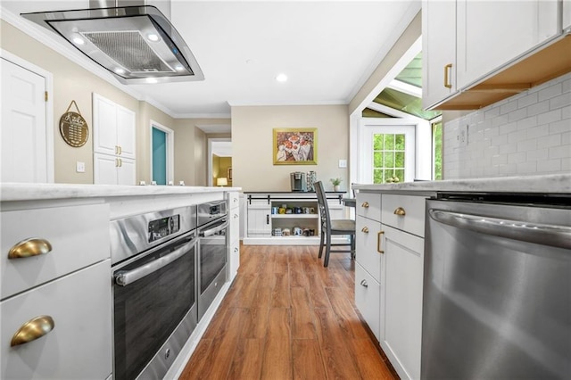 kitchen featuring crown molding, decorative backsplash, wood finished floors, light countertops, and appliances with stainless steel finishes
