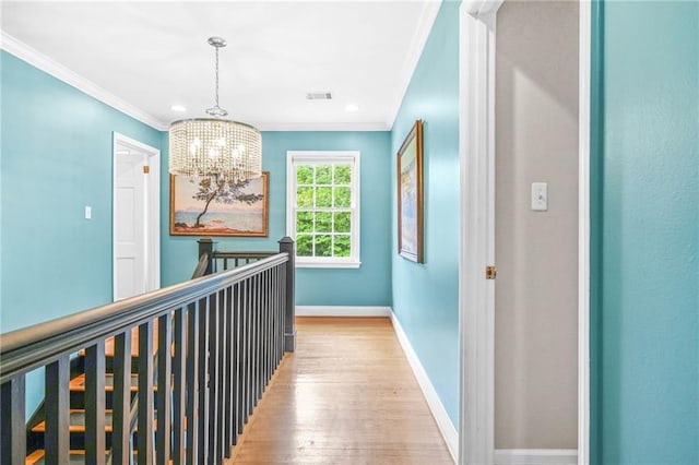 corridor with crown molding, light wood-type flooring, visible vents, baseboards, and a chandelier