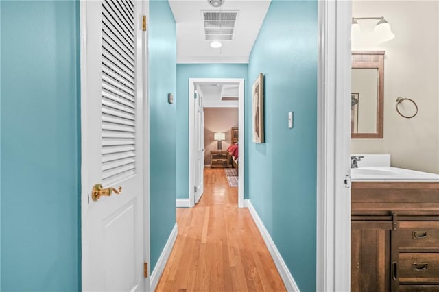 hall with a sink, light wood-style flooring, baseboards, and visible vents