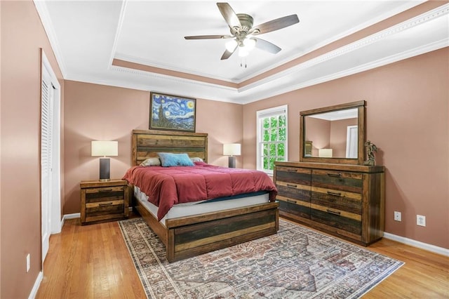 bedroom featuring baseboards, light wood-style flooring, a raised ceiling, and ornamental molding