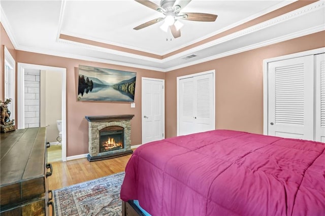 bedroom featuring ornamental molding, a raised ceiling, multiple closets, and wood finished floors