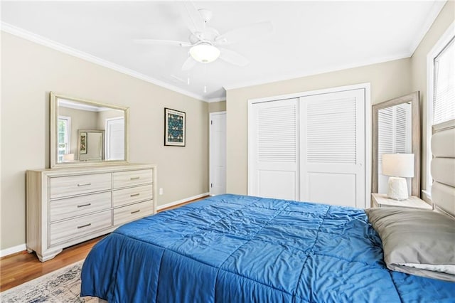 bedroom with a closet, wood finished floors, ornamental molding, a ceiling fan, and baseboards
