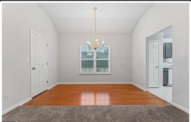 unfurnished dining area featuring a notable chandelier, lofted ceiling, carpet flooring, wood finished floors, and baseboards