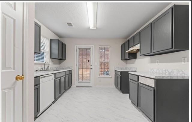 kitchen featuring visible vents, dark cabinets, white dishwasher, light countertops, and a sink