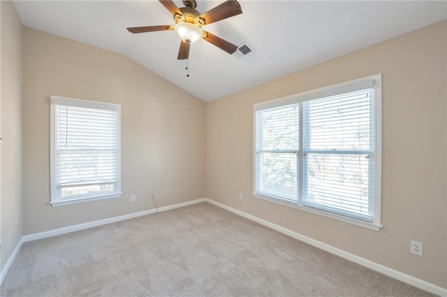 spare room featuring plenty of natural light, light colored carpet, visible vents, and vaulted ceiling