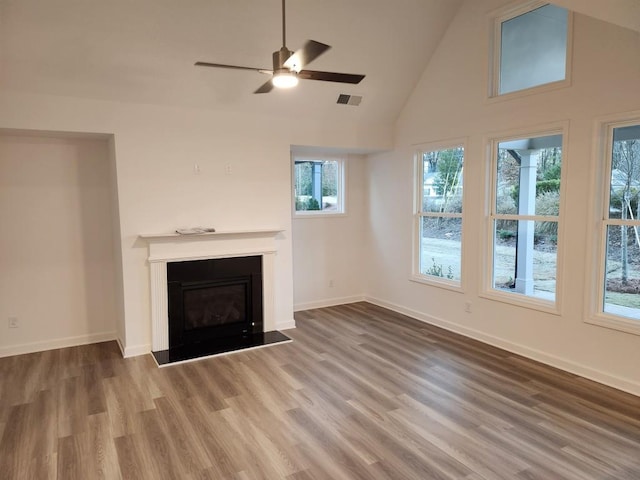 unfurnished living room featuring hardwood / wood-style flooring, high vaulted ceiling, plenty of natural light, and ceiling fan