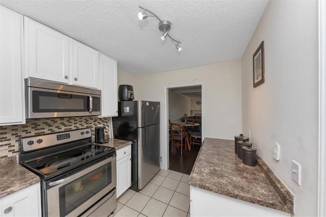 kitchen featuring light tile patterned floors, appliances with stainless steel finishes, white cabinetry, tasteful backsplash, and a textured ceiling