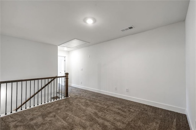 unfurnished room with attic access, baseboards, visible vents, and dark carpet