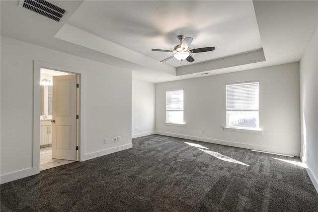 unfurnished bedroom featuring carpet, visible vents, baseboards, ensuite bathroom, and a raised ceiling