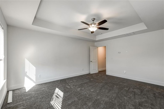 spare room with dark colored carpet, baseboards, a raised ceiling, and a ceiling fan