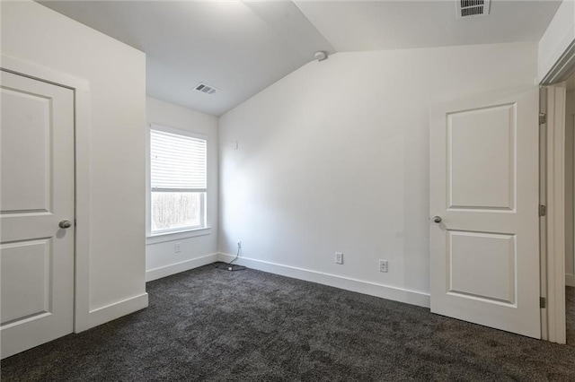 empty room featuring dark colored carpet, visible vents, lofted ceiling, and baseboards