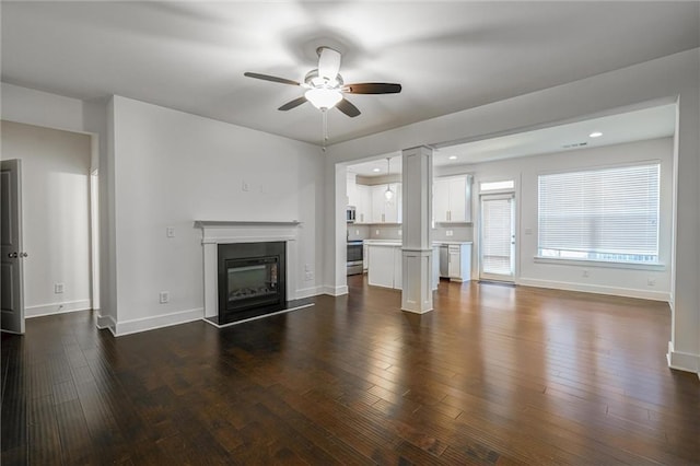 unfurnished living room with a glass covered fireplace, baseboards, a ceiling fan, and dark wood-style flooring