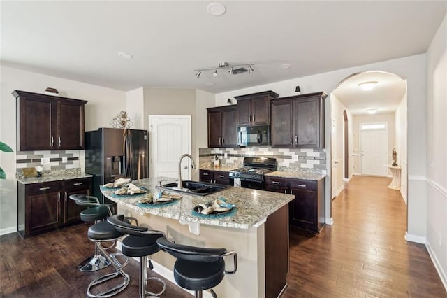 kitchen with sink, a kitchen breakfast bar, an island with sink, light stone countertops, and black appliances