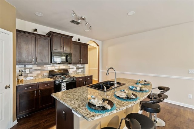 kitchen with sink, light stone counters, a kitchen breakfast bar, an island with sink, and black appliances