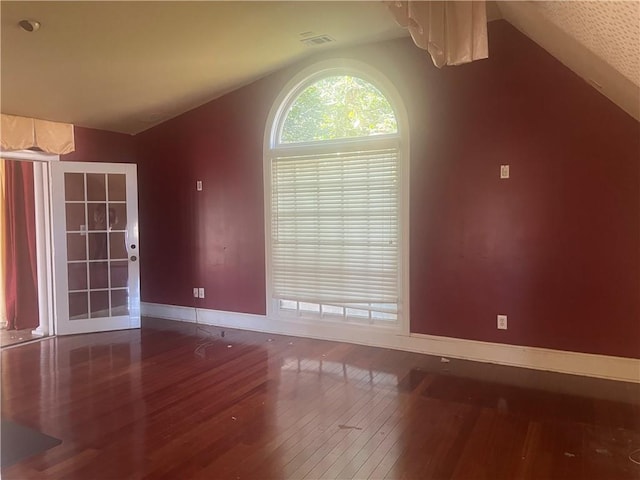 unfurnished room with vaulted ceiling, wood finished floors, baseboards, and visible vents