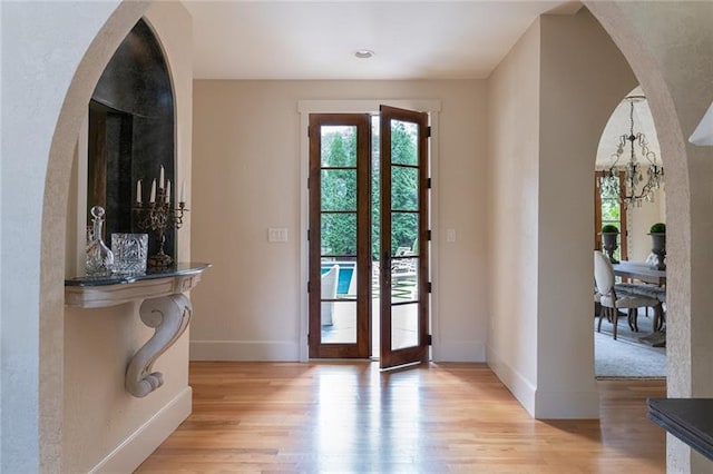 doorway to outside featuring light wood-type flooring, an inviting chandelier, and french doors