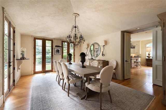 dining space featuring hardwood / wood-style flooring, a textured ceiling, a notable chandelier, and french doors