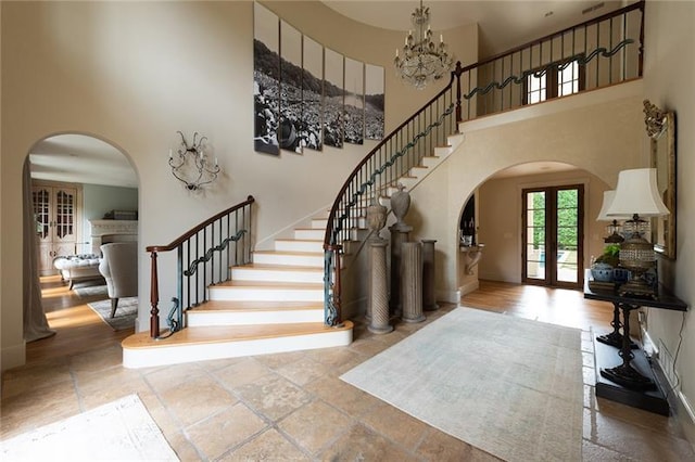 entrance foyer with a chandelier, a towering ceiling, wood-type flooring, and french doors