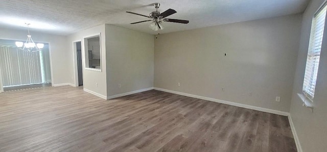 spare room with a textured ceiling, a wealth of natural light, ceiling fan with notable chandelier, and hardwood / wood-style floors