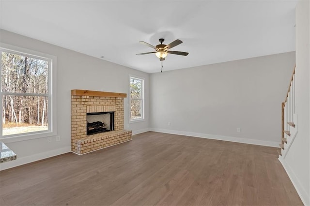 unfurnished living room featuring hardwood / wood-style flooring, a brick fireplace, and ceiling fan