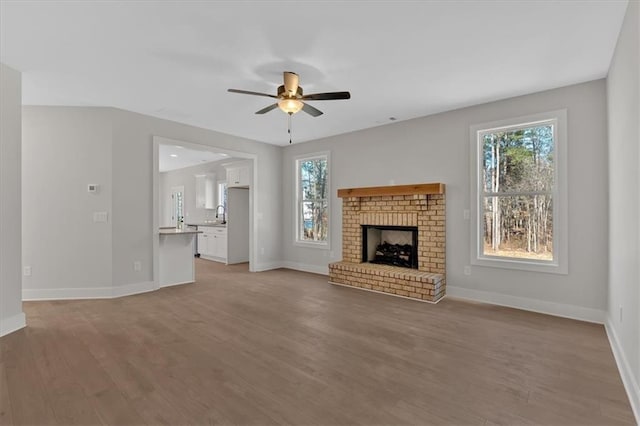 unfurnished living room featuring ceiling fan, light wood-type flooring, sink, and a fireplace