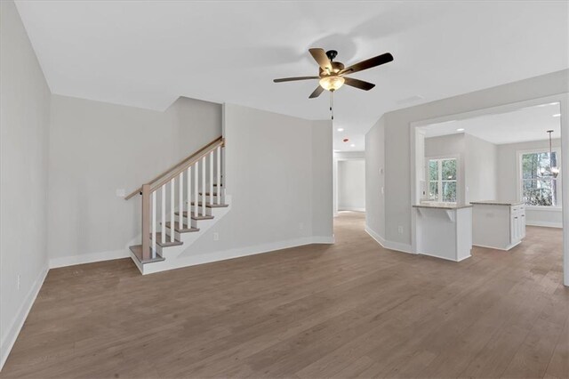 unfurnished living room with ceiling fan with notable chandelier and light hardwood / wood-style floors