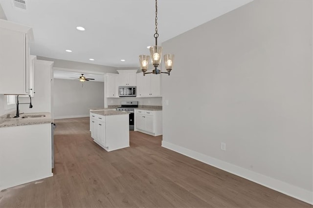 kitchen with appliances with stainless steel finishes, pendant lighting, white cabinetry, sink, and a center island