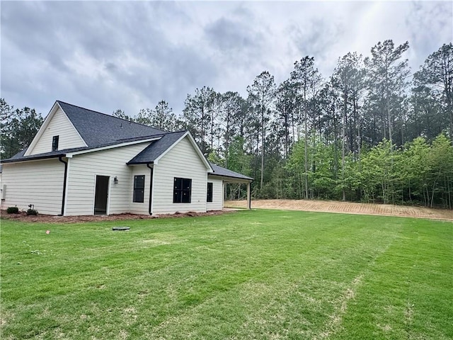 rear view of house featuring a lawn and a shingled roof